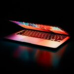 Laptop partially opened, emitting vibrant multicolored lights in dark setting.